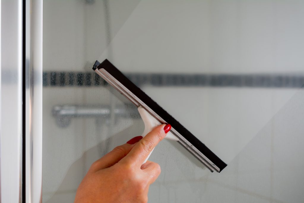 Someone uses a squeegee to clean their shower screen 