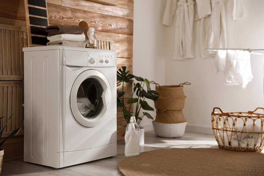White washing machine sits in a clean room with plants and washing baskets