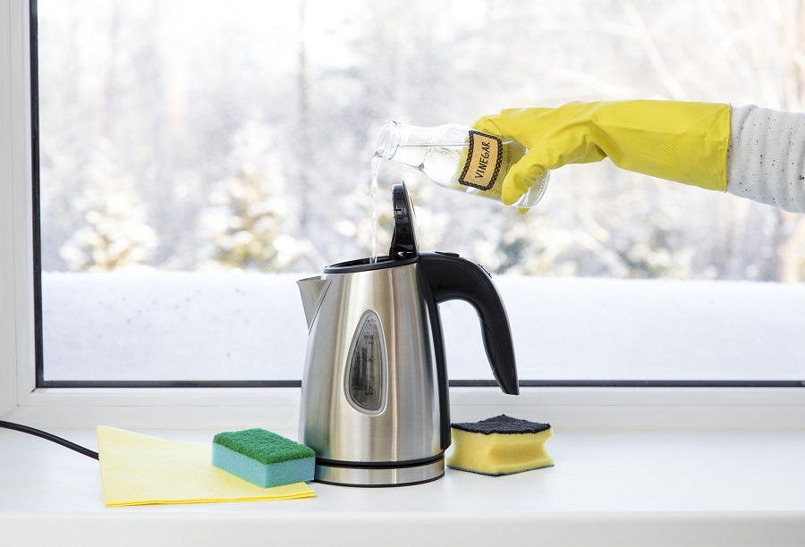 Someone in yellow rubber gloves descales a kettle by pouring vinegar into it