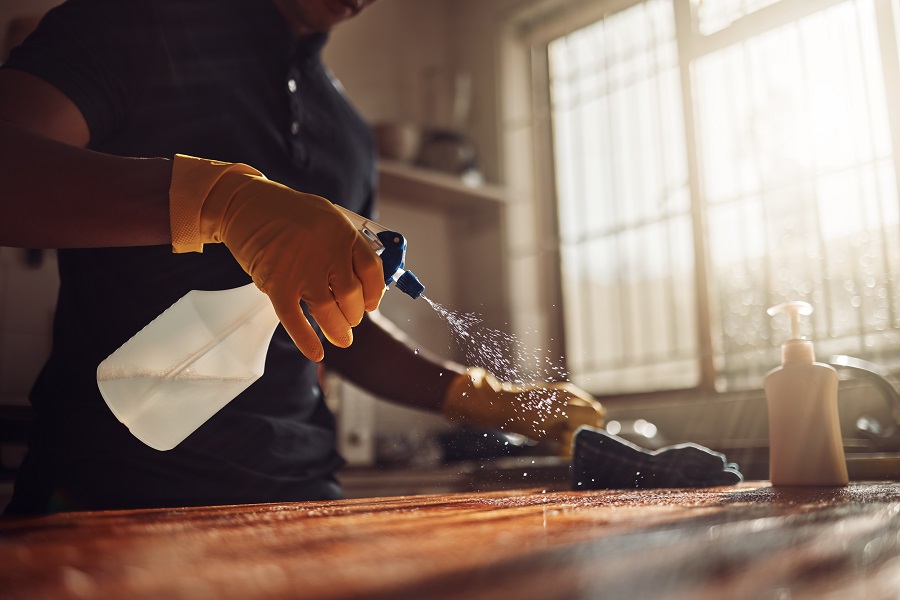 man spraying surfaces at home wearing gloves